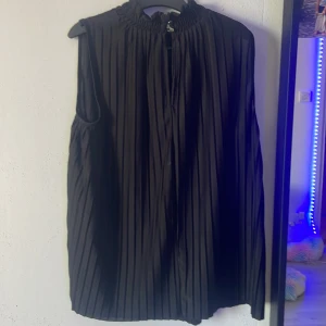 Plisserad svart väst/blus från H&M XS - Säljer en svart plisserad väst från H&M i storlek XS. Västen har hög krage med rynk och är ärmlös med en loose passform. Perfekt för att ge din outfit en cool och stilren touch.