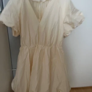 Ljus kortklänning med v-ringning - Supersöt ljus kortklänning med v-ringning och korta ärmar. Klänningen har en avslappnad passform med resår i midjan och lätt puffiga ärmar. Klänningen är helt ny och aldrig använd, endast testad
