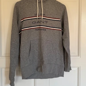 Grå hoodie från GANT med tryck - Grå hoodie från GANT med broderat tryck säljes då den inte används inte längre. Är storlek M men skulle säga att den är liten i storlek så passar även S.