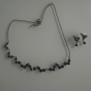 Set med halsband och örhängen med blå stenar - Snyggt smyckeset med halsband och matchande örhängen i silverfärgad metall. Båda delarna är dekorerade med glittrande blå stenar som ger en cool och elegant vibe