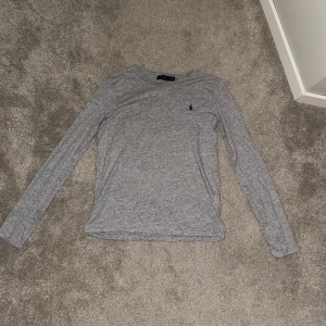 Grå långärmad tröja Polo Ralph Lauren - Snygg grå långärmad tröja från Polo Ralph Lauren med klassisk rund hals och broderad marinblå logga på bröstet. Tröjan är i mjuk bomull och har en clean, stilren look som passar perfekt till jeans eller kjol. Använd 3-5 ggr💕