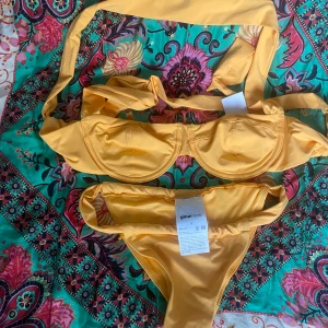 Orange bikini från Gina Tricot - Snygg orange  bikini från Gina Tricot med bygel-bh och breda axelband som knyts i nacken. Bikinitrosan har höga ben och smala sidor. Materialet är mjukt och stretchigt, perfekt för strandhäng eller poolparty. Den är helt ny med prislapp och därmed oanvänd. 