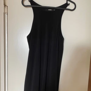 Svart ärmlös klänning  - En stilren svart klänning från Bik Bok i ärmlös modell med rund halsringning. Klänningen har en rak och enkel siluett, perfekt för dig som gillar minimalistisk stil. Mjuk och följsam känsla i materialet. Frakt tillkommer 