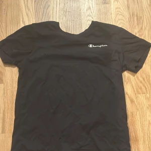 Champion t-shirt i bomull - Svart t-shirt från Champion i 100% bomull med klassisk passform. Diskret Champion-logga broderad på bröstet. Enkel och stilren design som funkar till allt. Perfekt för dig som gillar sportiga och avslappnade vibes.