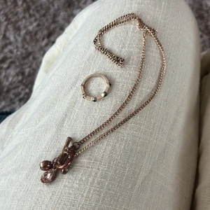 Guldfärgat halsband & ring med stenar - Säljer ett guldfärgat halsband med kedja och tre droppformade hängen i rött, rosa och transparent. Halsbandet har en snygg toggle-låsning. Till det ingår en matchande guldfärgad ring med små svarta stenar runt om. Perfekt för dig som gillar stilrena smycken med en twist. Aldrig använd 