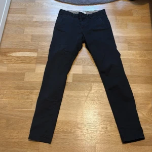 Svarta super slim chinos från Barton - Svarta chinos från Barton i super slim fit-modell. Byxorna har klassisk design med snedställda fickor fram och raka ben. Perfekta för dig som gillar en smalare passform och stilren look.