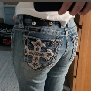 Blå miss me jeans  - Snygga ljusblå jeans från Miss Me med broderade kors på bakfickorna och små slitna detaljer framtill. Jeansen har låg midja och är bootcut. Den enda defekten som finns syns på sista bilden. 