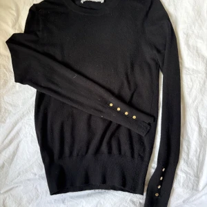 Svart stickad tröja från Zara - Svart stickad tröja från Zara i slim fit med rund halsringning och långa ärmar. Snygga guldfärgade knappar. Ett litet hål som knappt syns Pris kan diskuteras
