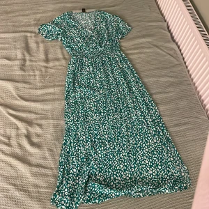 Grön blommig maxiklänning från SHEIN - Snygg långklänning i grönt med vitt blommigt mönster. Klänningen har korta ärmar, v-ringning och markerad midja. 