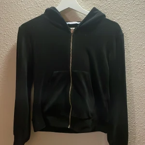Svart hoodie med dragkedja från 157 - Svart kofta från lager 157 i storlek XS. Klassisk modell med huva, hel dragkedja framtill och en stor magficka. Långärmad och i mjukt material, perfekt för chill dagar eller när du vill ha en enkel och stilren look.