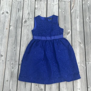 Blå ärmlös klänning Tommy Hilfiger - Supersöt blå klänning från Tommy Hilfiger med ärmlös design och markerad midja. Klänningen har ett vackert strukturerat tyg med blommiga detaljer och knappar i ryggen. Perfekt för dig som vill sticka ut med en klassisk men trendig look.