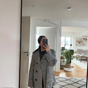 Hundtandsmönstrad Skepparkavaj/kort kappa med bälte  - Säljer en snygg svartvit skepparkavaj i hundtandsmönster med dubbelknäppning och bälte i midjan. Jackan har bred krage, stora knappar och klassisk passform. Passar allt mellan XS-M beroende på önskad passform (jag brukar ha XS-S)