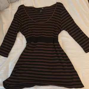 Randig lång tröja från H&M med knyt - Säljer en brun och svart randig lång tröja från H&M med trekvartsärm och snygg knytning i midjan. Klänningen har en rundad urringning och är tillverkad i ett mjukt, stretchigt material som sitter bekvämt och snyggt. Tröjan är köpt på plick☺️tröjan har storlek M men den passar mig som har s och även xs också eftersom att man kan knyta där back. Har använt typ 1 gång