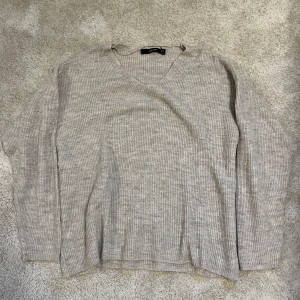 Beige ribbad stickad tröja Vero Moda - Mysig beige stickad tröja från Vero Moda i ribbat material. Tröjan har v-ringning och långa ärmar. Den är i ett fint skick.