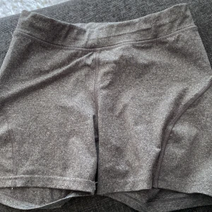 Grå träningsshorts  - Gråa träningsshorts  i stretchigt och mjukt material. De har en midwaist passform och är perfekta för gymmet eller löprundan. Snygg, enkel design utan mönster och med diskret logga bak i midjan. Sitter tajt och följer kroppen.