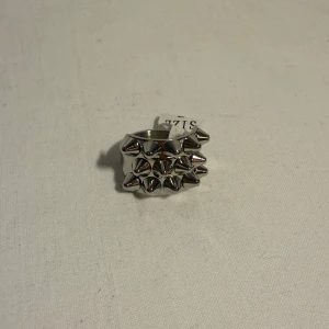 Silvrig ring med nitar, storlek 7 - Cool och chunky ring i silverfärgad metall med flera spetsiga nitar framtill. Ringen har en bred design och passar perfekt för dig som vill sticka ut med en edgy accessoar. Storlek 7.
