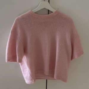 Ljusrosa stickad tröja Gina Tricot strl M - Superfin ljusrosa stickad tröja från Gina Tricot i kortare modell. Tröjan har korta ärmar, rund halsringning och ribbade kanter. Perfekt för lager-på-lager och ger en söt vibe till din outfit.