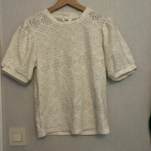 Vit spetsblus från Object XS - Superfin vit blus från Object i storlek XS. Blusen har korta puffärmar och är helt täckt av broderad spets med snyggt hålmönster. Perfekt för dig som gillar romantisk och luftig stil. Rund halsringning och mjukt bomullsmaterial.