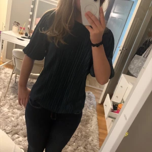 Mörkgrön plisserad blus - Säljer en snygg mörkgrön plisserad blus som har korta puffärmar och rund halsringning. Materialet är glansigt och ger en cool effekt med de smala plisserade vecken. Passar både till vardag och till fest