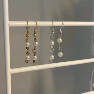 Hängande örhängen med pärlor - Två par hängande örhängen med kedjor och vita pärlor. Ena paret har guldfärgade detaljer och det andra har silverfärgade detaljer. Perfekta för att ge en elegant touch till din stil. 1 par för 35kr och båda för 55kr