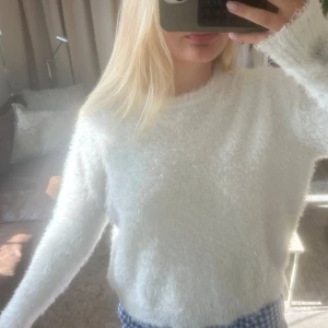 Vit fluffig stickad tröja - Supermjuk och fluffig vit stickad tröja med lång ärm och rund hals. Perfekt för dig som gillar en cozy vibe och vill ha något riktigt gosigt till höst och vinter. Enkel att matcha med både jeans och kjol.