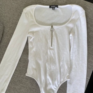 Vit långärmad topp från Missguided - Vit ribbad långärmad topp från Missguided med rundad fyrkantig urringning och en snygg dragkedja framtill med ringdetalj. Tight passform och stretchigt material som sitter snyggt på kroppen. Perfekt att styla med jeans eller kjol.