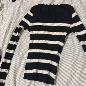 Randig ribbad långärmad tröja - Säljer en svart och vit randig ribbad tröja med lång ärm och fyrkantig halsringning. Tröjan är tight i modellen och har en stretchig, stickad känsla. Perfekt för dig som gillar klassiska ränder och vill ha en stilren look.