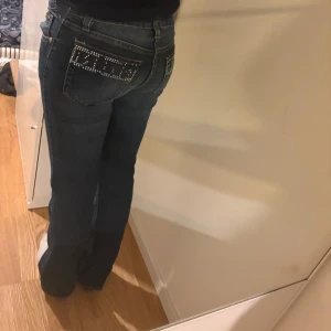 Dolce & Gabbana jeans - Mörkblå bootcut jeans från Dolce & Gabbana med låg midja och snygga strassdetaljer på bakfickorna. Tyvärr har några av paljetterna lossnat. Midjemått 35, innebenslängd 78. Perfekt för dig som vill ha nått extra💗