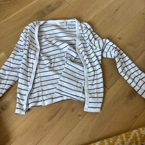 Vit och svart randig kofta Kappahl - Vit kofta från Kappahl med svarta horisontella ränder. Långärmad och med knappar framtill. Tunn och mjuk känsla, perfekt för lager-på-lager. Klassisk och enkel design som funkar till många olika stilar.