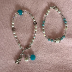 Pärlarmband med blå detaljer och berlock - Fint armband med vita pärlor, turkosa och genomskinliga glaspärlor samt en söt silverfärgad björnberlock. Armbandet har ett smidigt klolås och extra hängande pärlor i blått och vitt. Perfekt accessoar för att lyfta din stil.