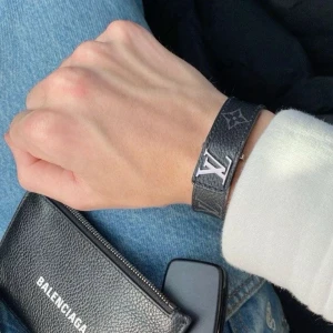 Lv armband  - Stilrent Ny! svart armband från Louis Vuitton i läder med klassiskt monogrammönster och silverfärgad LV-logga. Justerbar längd och diskret design som ger en lyxig touch till din outfit. Kommer ej! originalbox och dustbag.