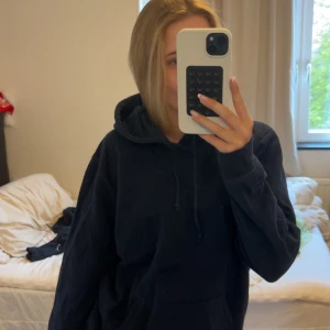 Mörkblå hoodie med stjärnor i silver - Mysig mörkblå hoodie med huva och snörning. På ryggen finns stora silvriga stjärnor som ger en cool vibe. Tröjan har känguruficka framtill och en relaxed, lite oversized passform. Perfekt för chill dagar eller när du vill sticka ut lite extra.