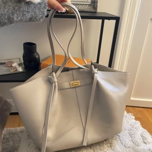 Väska från Gina tricot - Stilren beige axelväska i slätt skinn med långa axelband och snyggt guldfärgat spänne framtill. Väskan är från Gina tricot och är i den större modellen som på bilden, knappt använd 💖