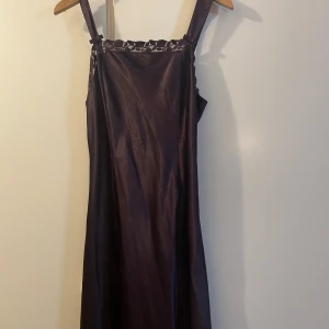 Mörklila nattlinne från Lindex 38/40 - Snyggt nattlinne i mörklila från Ella May, Lindex. Klänningen har breda axelband och vacker spetsdetalj upptill med blommönster. Materialet är glansigt och känns lyxigt, perfekt för dig som vill sticka ut.