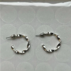 Silvriga tvistade örhängen hoops - Säljer ett par snygga silvriga örhängen i tvistad design. De är små hoops med coolt vridet utseende som ger en modern touch till din stil. Perfekta för dig som gillar minimalistiska men ändå unika smycken.