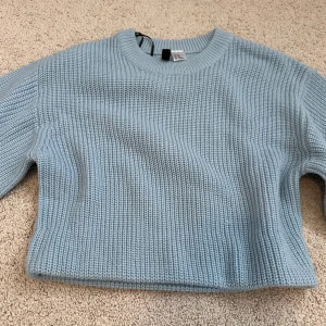 Ljusblå stickad croppad tröja från H&M Divided - Säljer en ljusblå stickad croppad tröja från H&M Divided. Tröjan har lång ärm, rund halsringning och en chunky stickad struktur. Perfekt för lager-på-lager och enkel att styla till olika outfits.