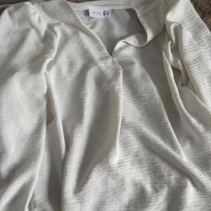 Vit långärmad topp från VILA - Säljer en stilren vit långärmad topp från VILA. Toppen har en enkel design med rund halsringning och är tillverkad i ett mjukt material som känns skönt mot huden. Perfekt att matcha med jeans eller kjol.