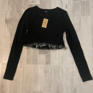 Svart croppad topp med pärlor - Svart långärmad  topp med dekorativa pärlor längs nederkanten. Aldrig använd.