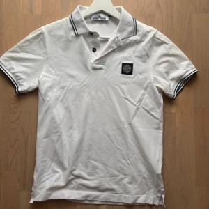 Vit piké från Stone Island - Vit pikétröja från Stone Island med svart compass -patch på bröstet. Tröjan har svarta ränder på krage och ärmslut samt två knappar vid halsen. Perfekt för en stilren look. Mycket fint skick, inga defekter. Uppkollad och äkta. Bara att höra av sig vid frågor!