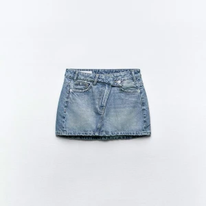 Blå jeanskjol från Zara - Säljer en klassisk blå jeanskjol från Zara med femficksmodell och bälteshällor. Kjolen är kort och har en rak passform, perfekt till sommaren. Stängs med knapp och dragkedja framtill.