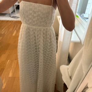 Vit långklänning med spets och snörning i ryggen - Säljer en vit långklänning med smala axelband och vackert blommigt spetsmönster. Klänningen har öppen rygg med snygg snörning och markerad midja. Perfekt för sommarens speciella tillfällen! Endast använd 1 gång!😍