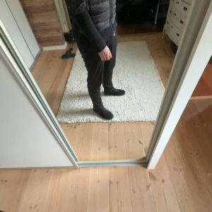 Svart dunväst från Moncler - Säljer en svart dunväst från Moncler med klassisk design. Västen har hög krage och dragkedja framtill. Perfekt för lager-på-lager och passar till många olika stilar. Moncler-logga på insidan. Självklart äkta köpt i moncler i Stockholm. Storlek L passar XL tips köp storlek större än va du har för den e inte true to size