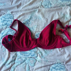 Röd ribbad bikiniöverdel - Säljer en snygg röd bikiniöverdel med ribbad struktur och knyt i ryggen. Bikinin har bygel och vita detaljer på insidan. Perfekt för sommaren och strandhäng!