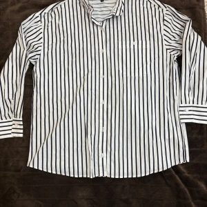 Vit och marinblå randig skjorta från H&M - Klassisk skjorta från H&M i vitt med marinblå ränder. Aldrig använt. Skjortan har lång ärm, bröstficka och knäppning framtill. Perfekt för en stilren och avslappnad look.