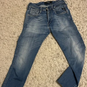 Blå Replay Anbass jeans - Säljer ett par klassiska blå jeans från Replay, modell Anbass. Jeansen har fem fickor, snygga slitningar och raka ben. De är 85cm långa med en lätt tvättad look.
