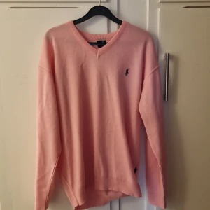 Ljusrosa tröja från Polo Ralph Lauren - Säljer en ljusrosa tröja från Polo Ralph Lauren med v-ringning och broderad logga på bröstet. Tröjan är i mjukt material och har långa ärmar samt ribbade muddar vid ärmslut och nederkant. Mycket bra skick . 