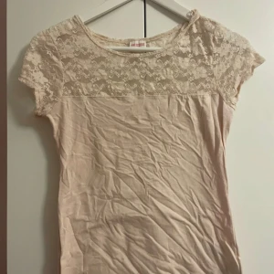 Beige topp med spetsdetaljer - Söt beige topp med korta ärmar och spets upptill. Spetsen har ett blommigt mönster som ger en romantisk känsla. Perfekt att matcha med jeans eller kjol för en stilren look.priset går att diskutera 🤍