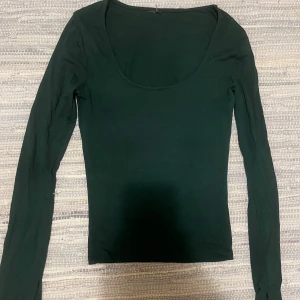 Mörkgrön långärmad topp med slits - Säljer en mörkgrön långärmad topp med rundad urringning och slits vid ärmslutet. Lappen är av men storleken är XS