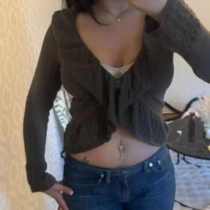 Olivgrön stickad tröja/kofta - Olivgrön stickad kofta med volangkant. Koftan har långa ärmar med breda muddar och fina stickade detaljer. Perfekt att slänga på sig över ett linne 😍