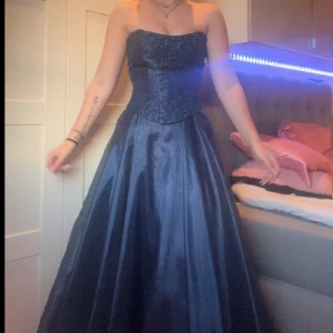 Mörkblå balklänning - Säljer en elegant mörkblå långklänning från Aspeed med vackert broderat upptill och smala axelband. Klänningen har utsvängd kjol och är tillverkad i glansig polyester. Perfekt för balen ! Man kan ha den antingen med banden eller utan o ha den som en tub kläning. Dragkedja bak🫶🏼💙